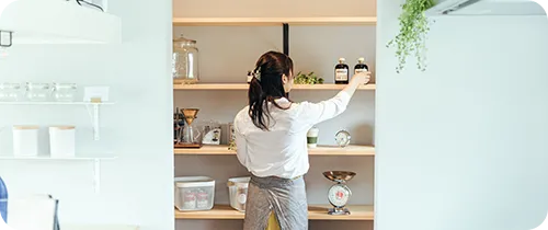 棚の整理をする、エプロンを付けた女性の後ろ姿